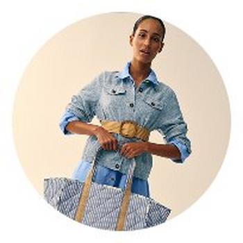 a woman in a blue linen dress and jacket holding a bag