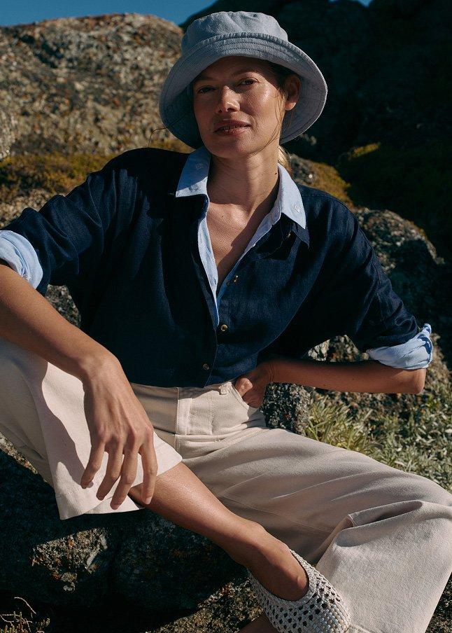 a woman sitting on a rock wearing a hat and a shirt