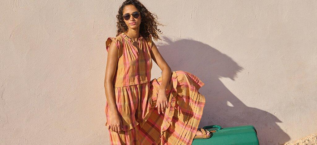 A female model posing in White Stuff's pink rosie check maxi dress. Copy reads free delivery over £70. Click to shop.