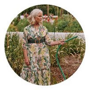 a woman in a dress watering a garden with a hose