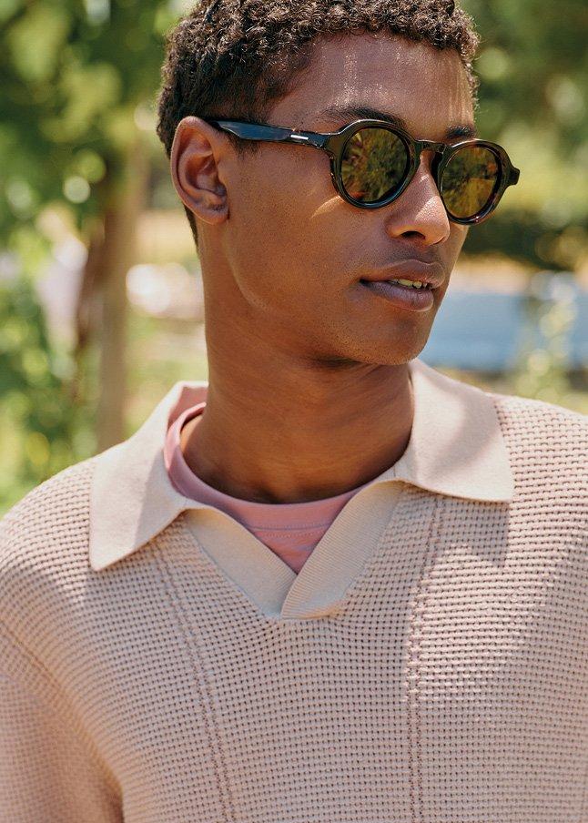 a man in a sweater and sunglasses standing in a park