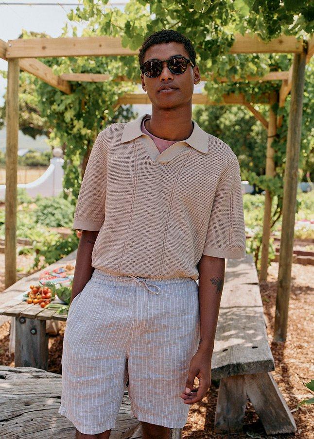 a man in a tan shirt and white shorts standing under a covered area