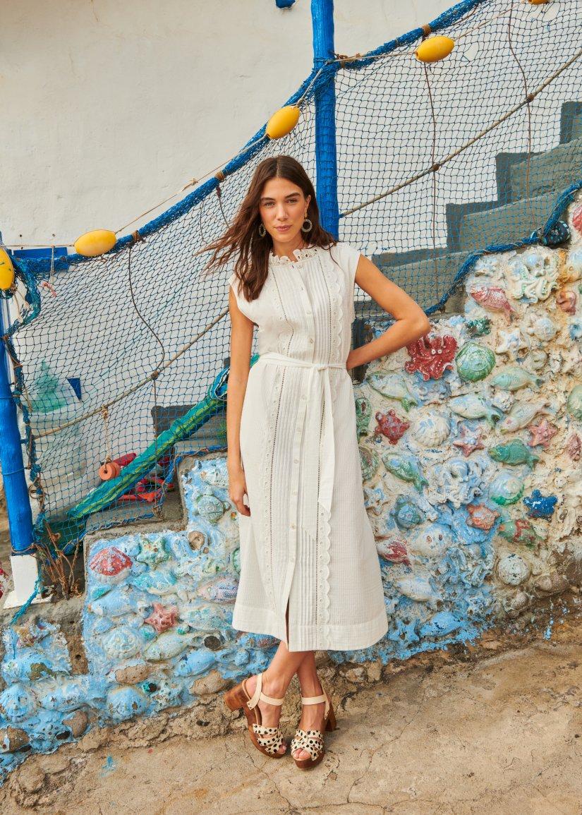 a woman in a white dress posing near a wall