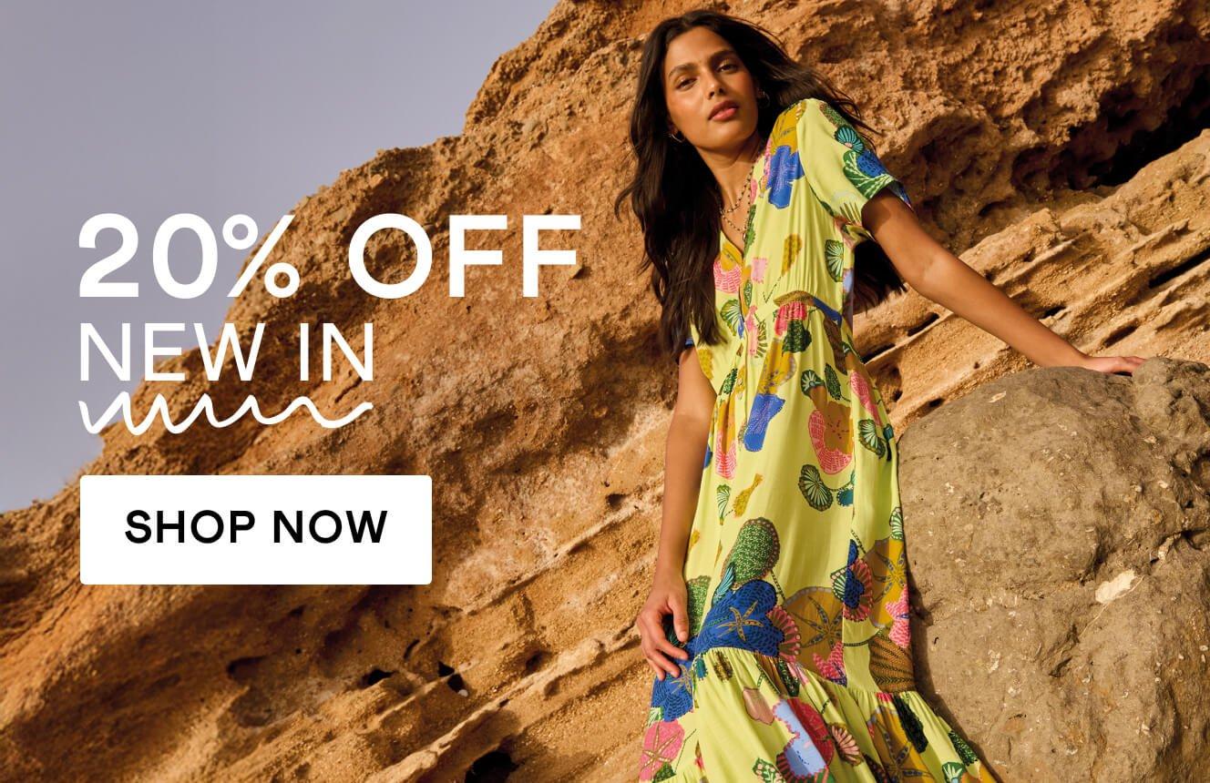 A woman wearing a lime green dress with geometric patterns, leaning on a rock in the desert, with the text "20% off new in", Click here to shop new in clothing. 
