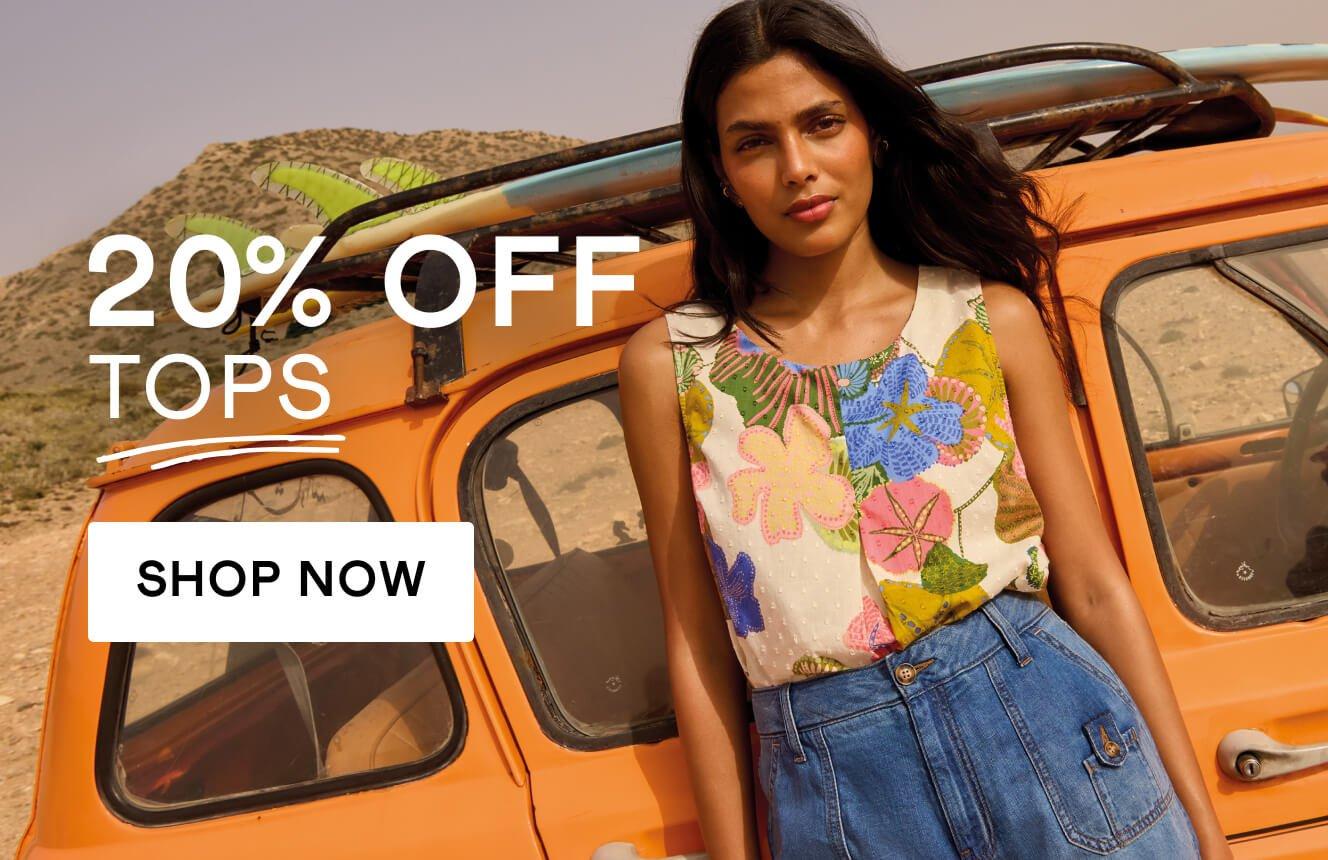 A woman wearing a floral printed top and blue denim sorts leaning on a yellow car, with the text "20% off tops", Click here to shop tops.