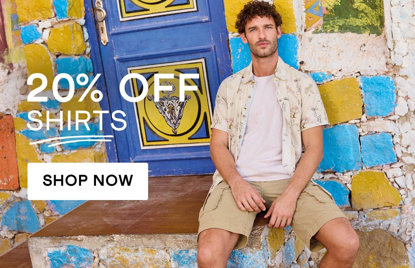 A man wearing a floral printed shirt and white tee standing in front of a colourful wall besid with the words "20% off Shirts" '. Click here to shop 20% off men's shirts.