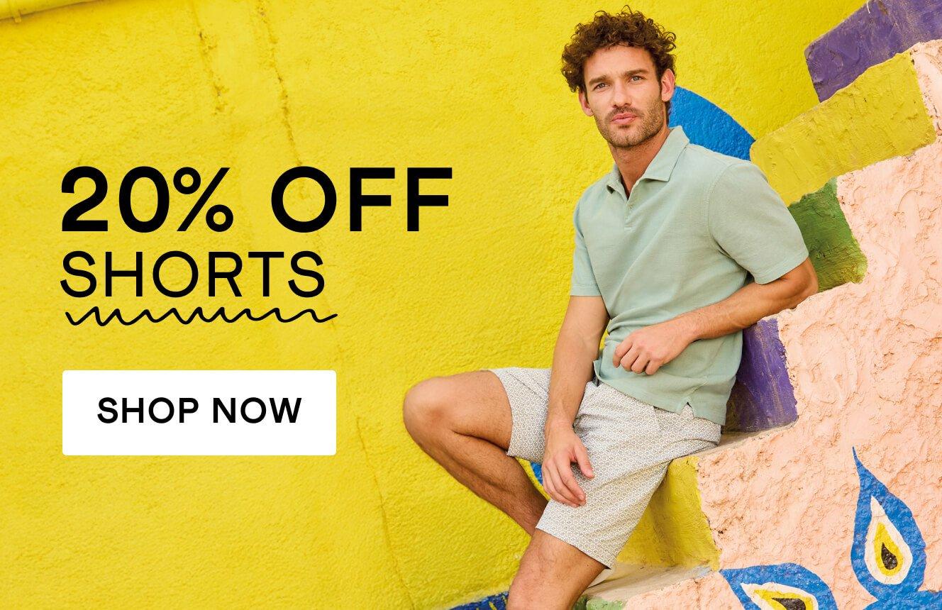 A man wearing a green polo and cream shorts sitting on steps, with the words "20% off Shorts" '. Click here to shop 20% off men's shorts.