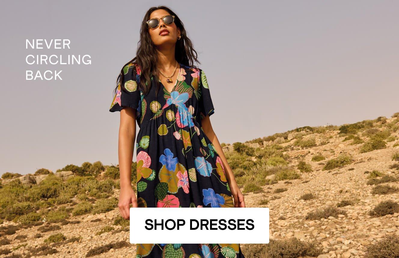 A woman wearing a black dress with geometric patterns in the desert, with the text "never circling back", Click here to shop dresses. 