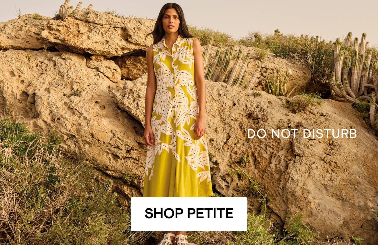 A woman wearing a yellow dress with a floral patters, standing on a box in the desert, with the text "do not disturb", Click here to shop petite sizes. 