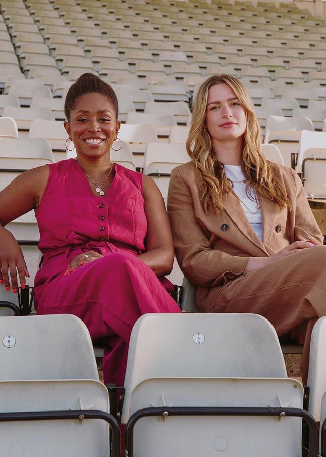 two women sitting on a row of empty seats at a stadium