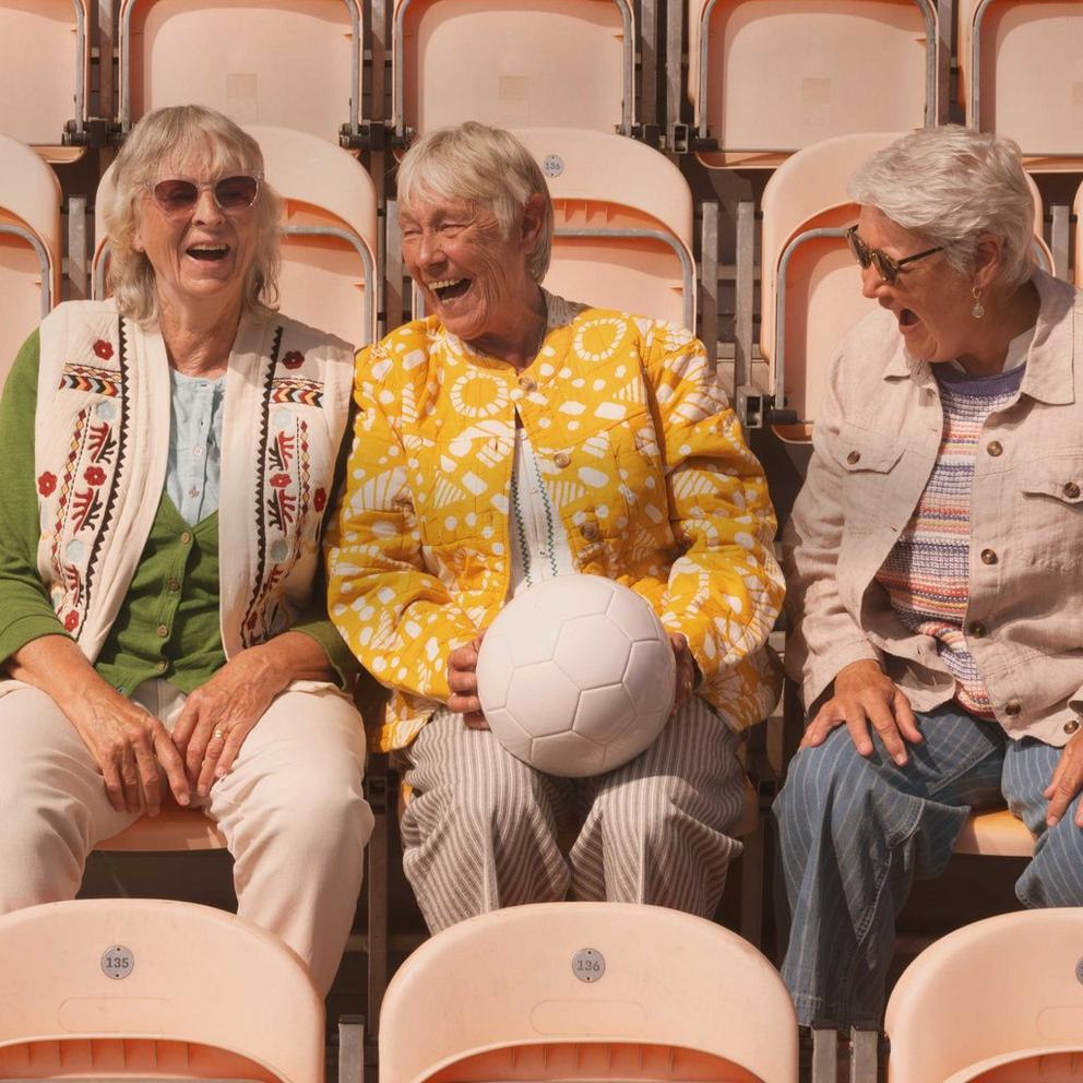 three women sitting in a stadium with a soccer ball