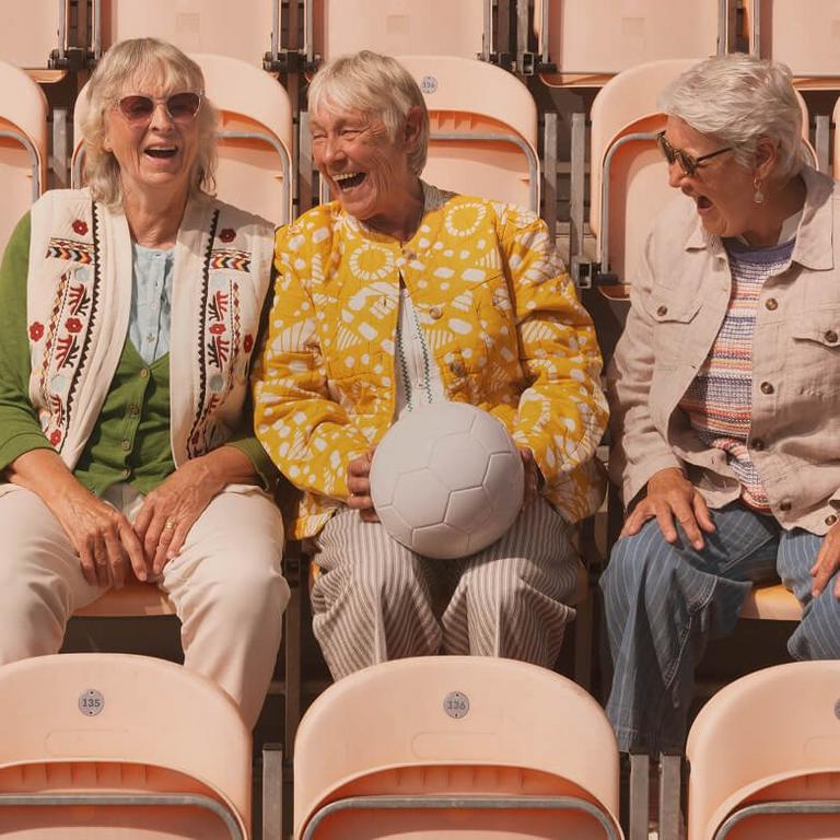 three women sitting in a stadium with a soccer ball