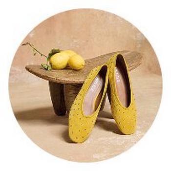 a pair of yellow shoes sitting on a wooden stool next to a lemon
