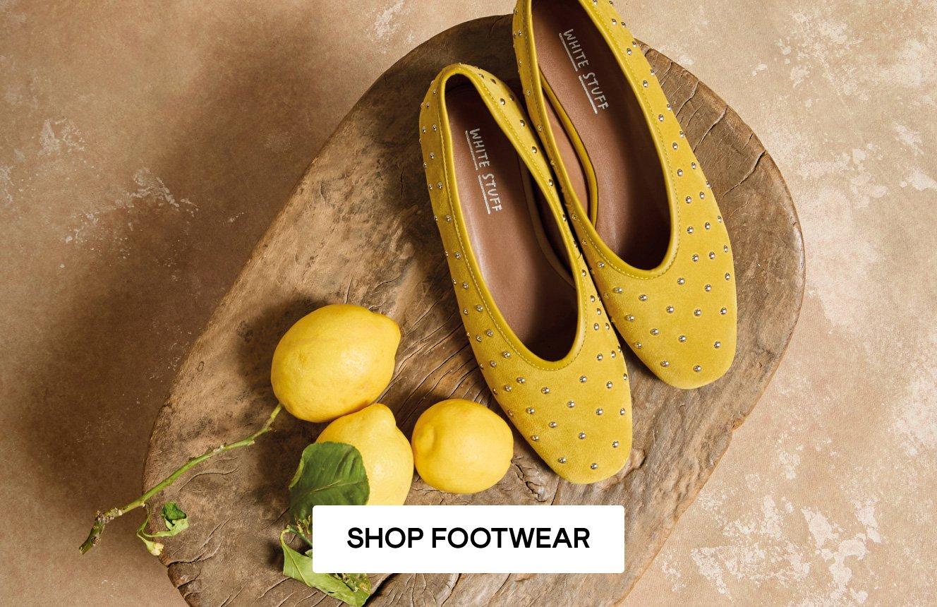 The yellow Boho Studded Ballerinas sitting on a chair next to 3 lemons.  Click here to shop footwear.