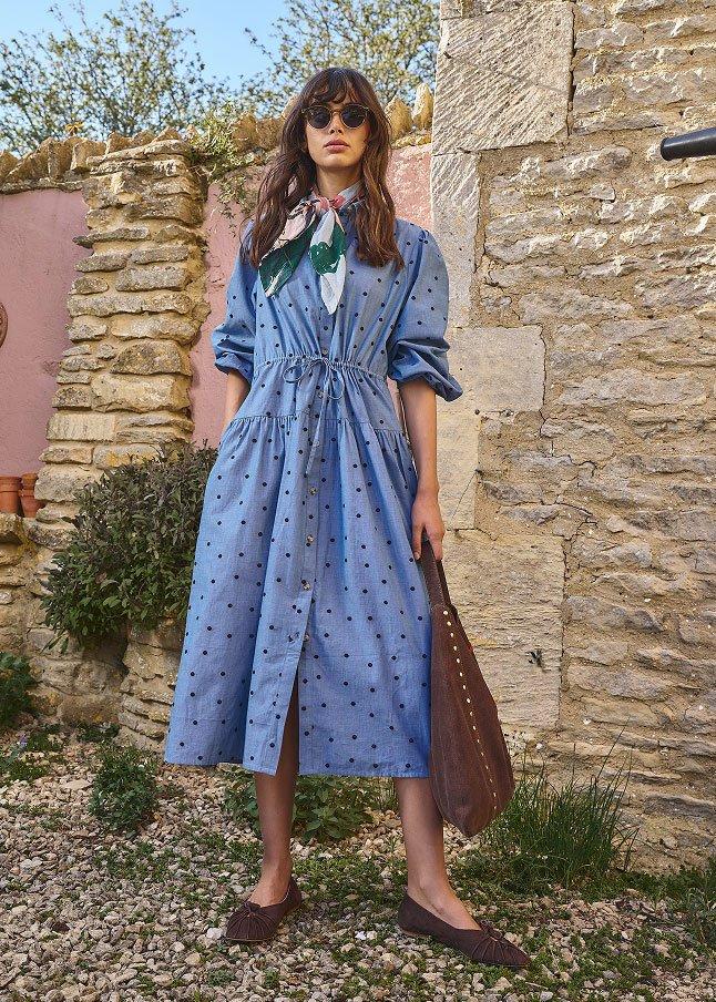 a woman in a blue dress and brown bag standing outside