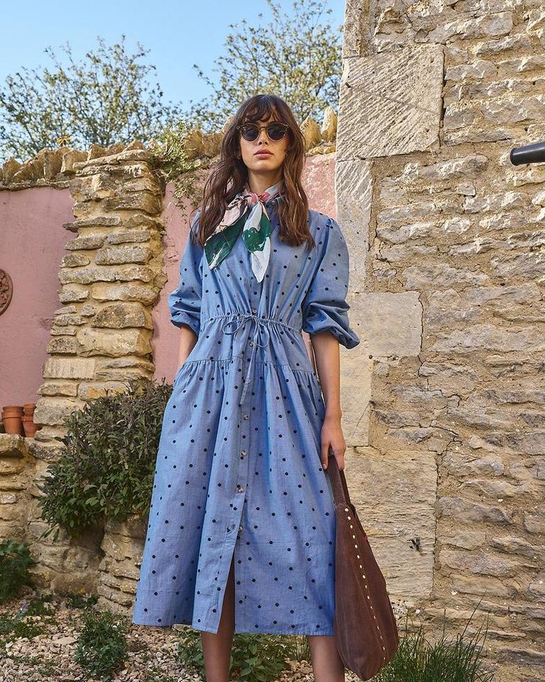 a woman in a blue dress and brown bag standing outside