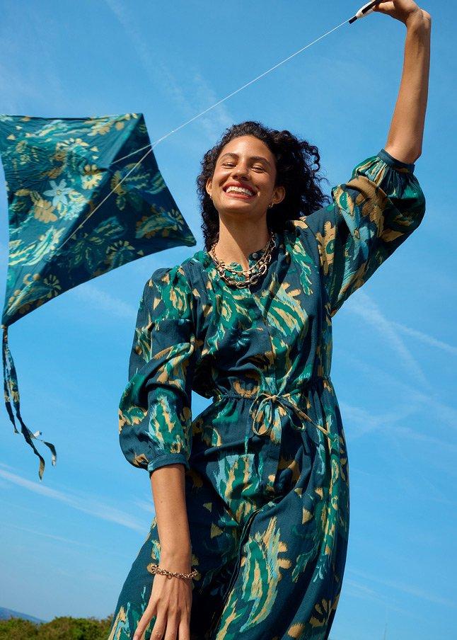 a woman in a green dress flying a kite in the sky
