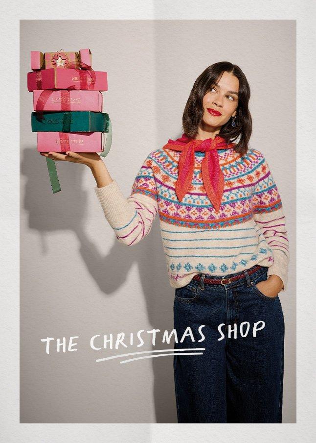 a woman holding up a stack of christmas presents