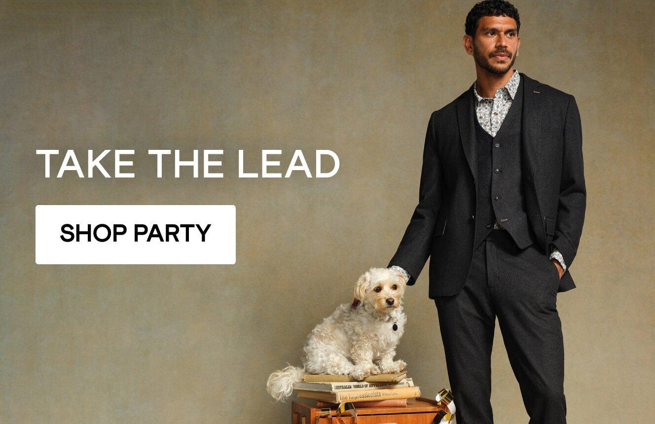 a man wearing a suit with a dog on a chair, click here to shop partywear