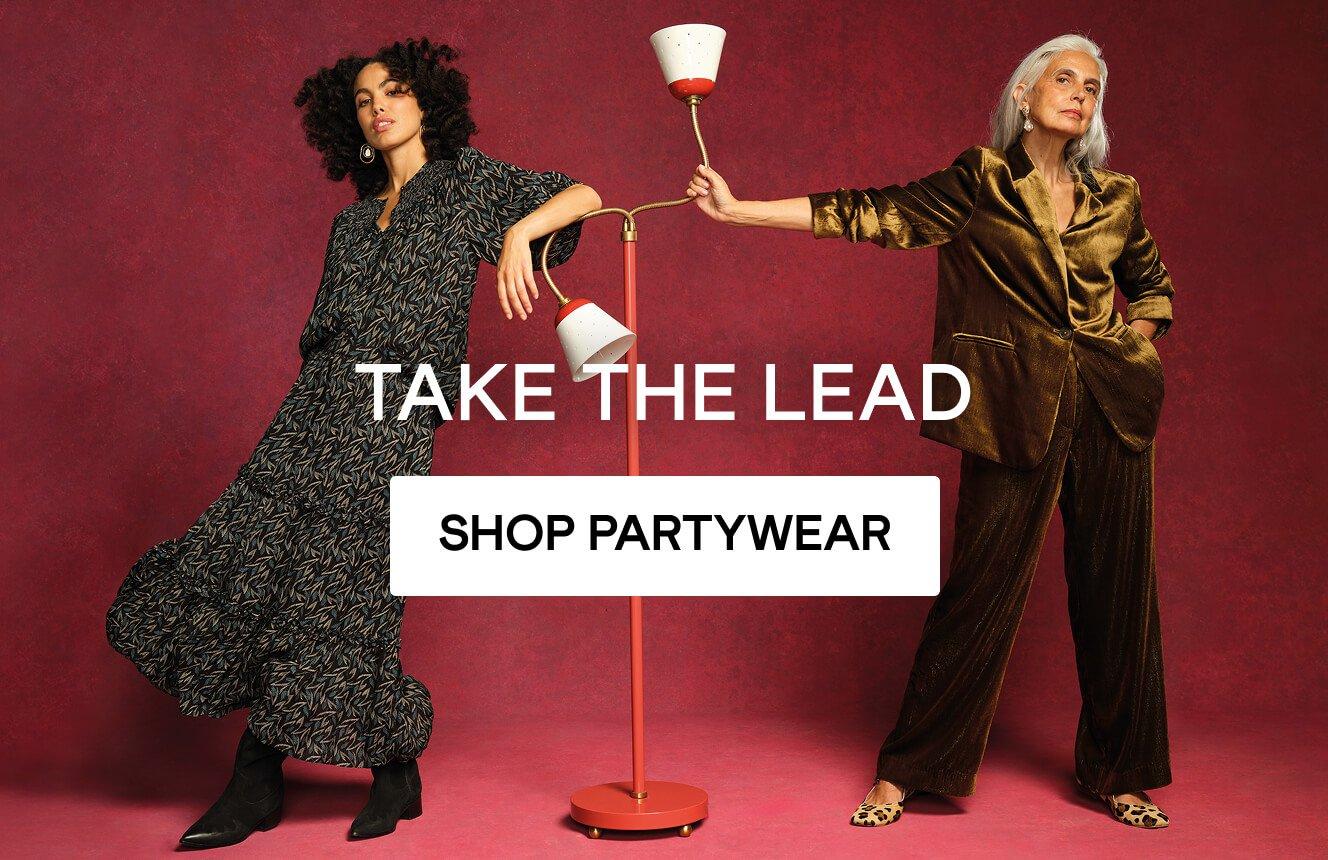 A woman wearing a pink linen Two women wearting party clothing, click here to shop more.and a black skirt with geometric patterns, lounging on a rock in the desert. Click here to shop linen.