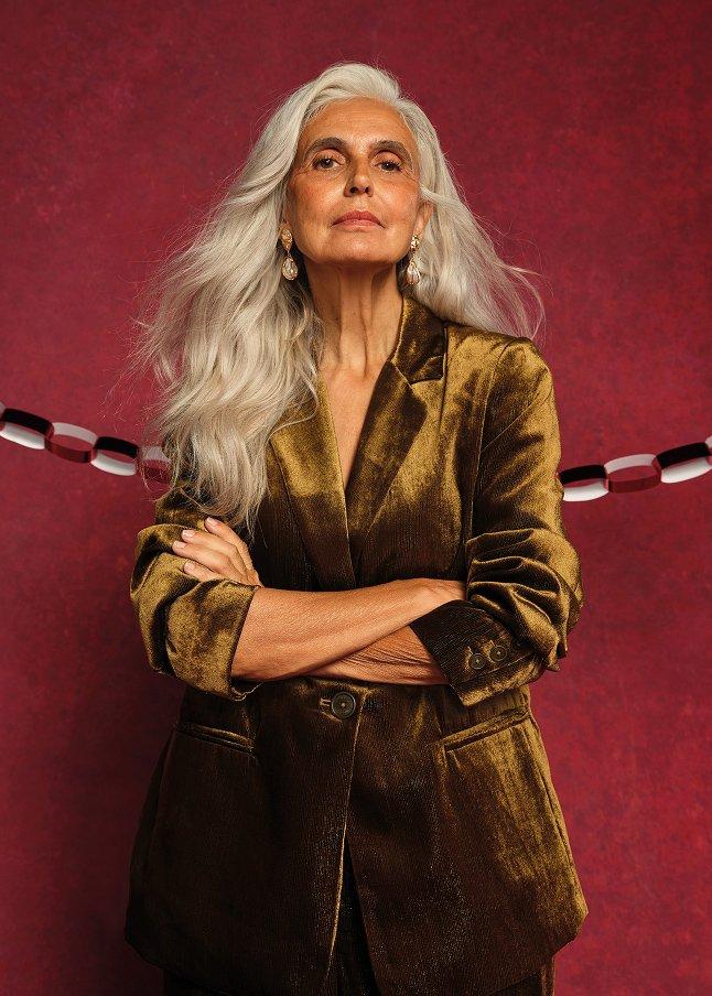 a woman with white hair and a gold jacket standing in front of a red rope
