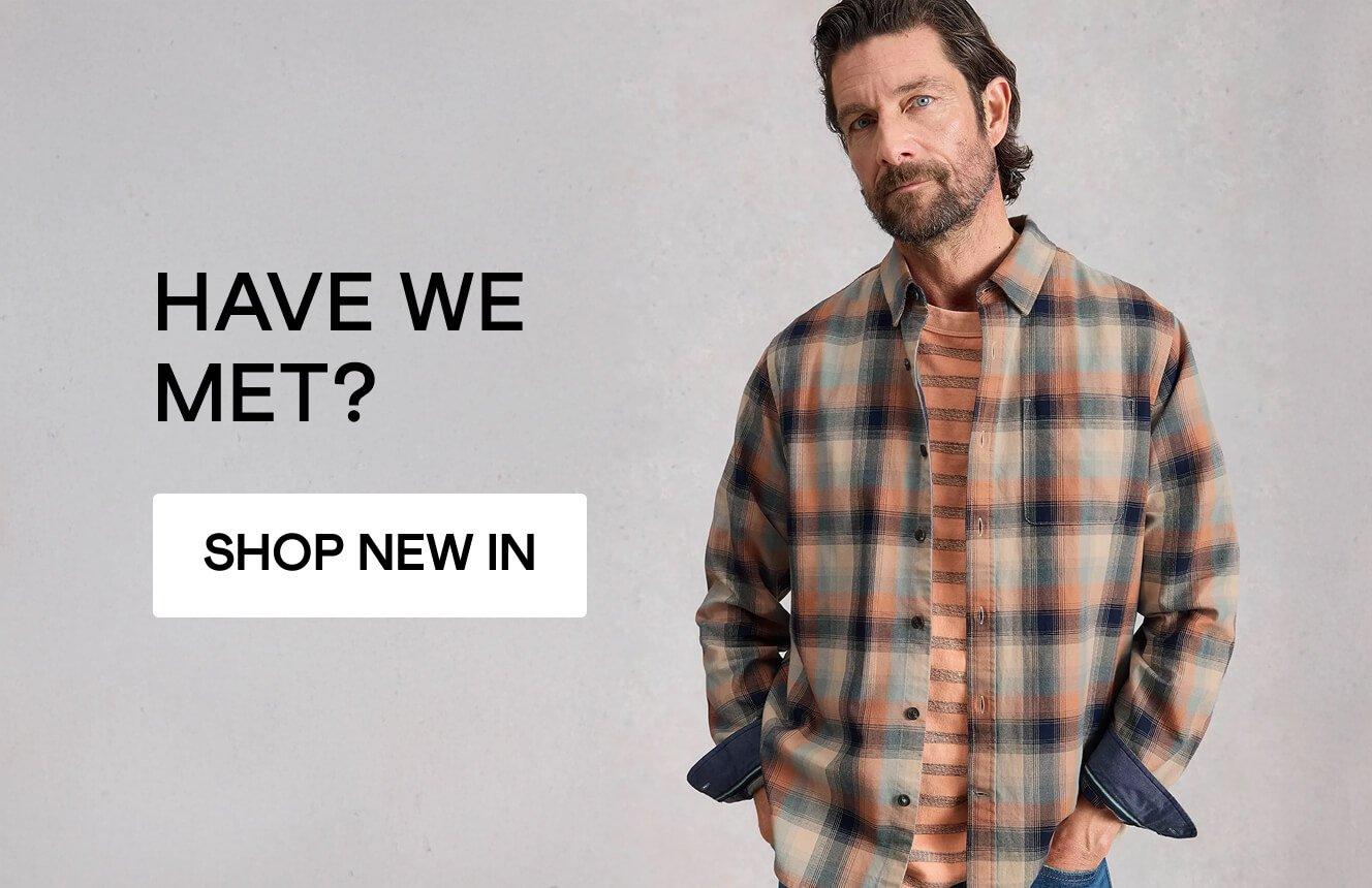 Man wearing a plaid button-up shirt with hands in pockets against a neutral background, with the text ‘Have we met?’ and a ‘Shop New In’ button.