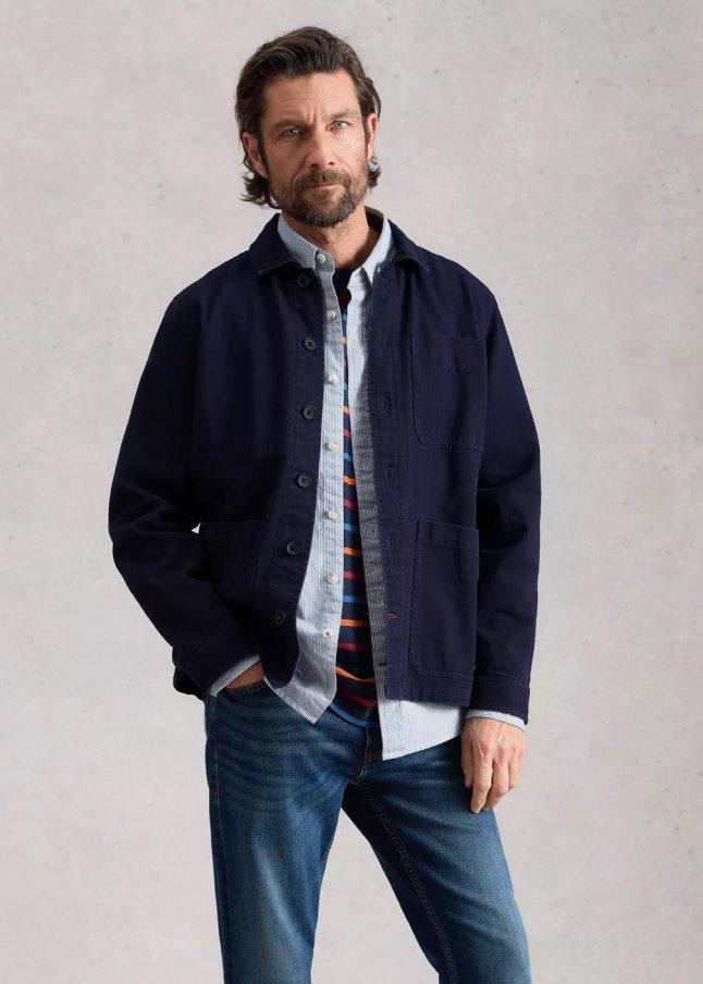 a man in a jacket and jeans standing with his hands on his hips