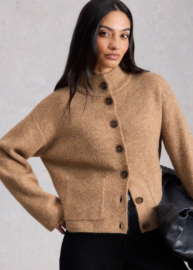 a woman in a tan sweater and black pants holding a purse