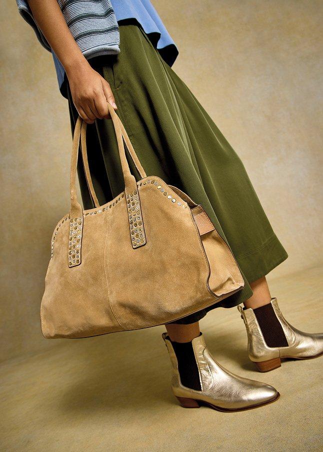 a woman in a skirt and boots holding a bag