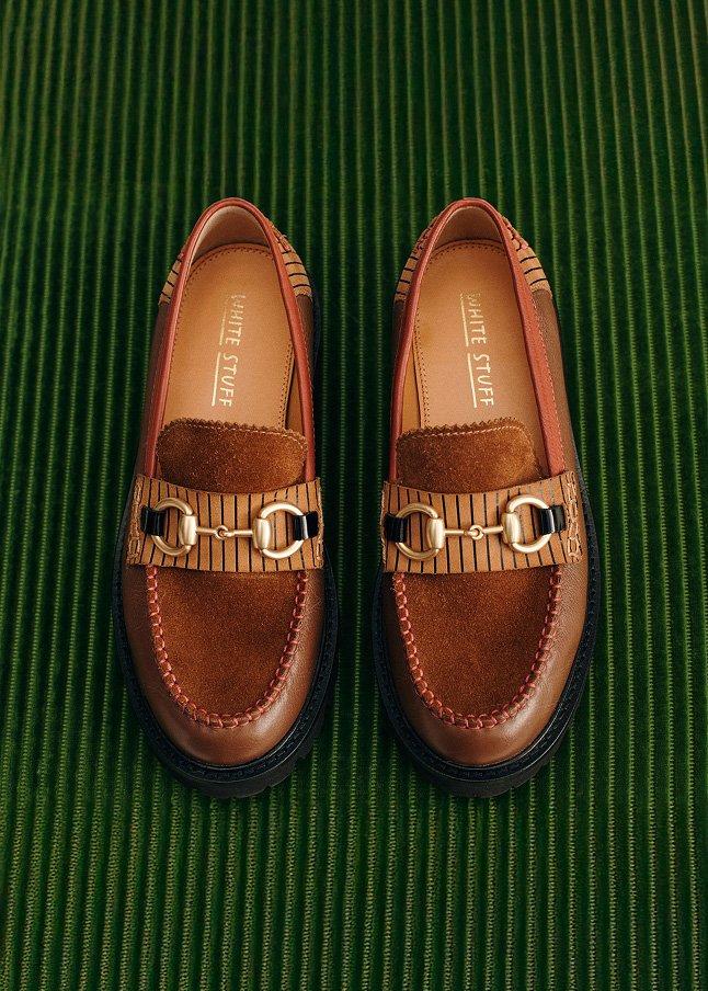 a pair of brown loafers with gold buckles on a green carpet
