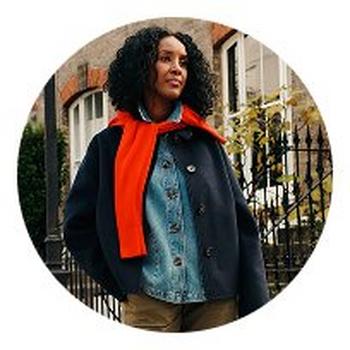 a woman in a jacket and scarf standing in front of a building