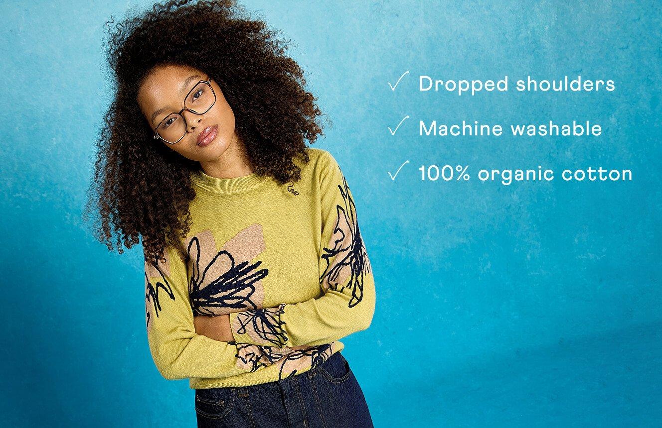 A woman wearing the Olive Jumper. Text on Image is "dropped shoulders, machine washable, 100% organic cotton".