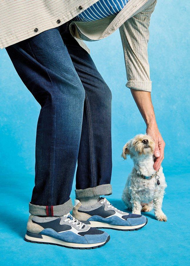 a man in jeans and sneakers petting a small dog