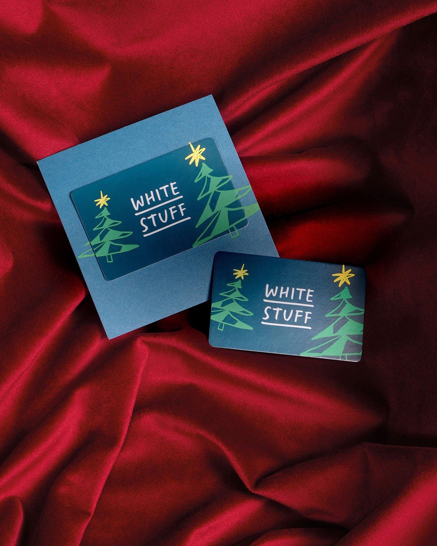 a white stuff gift card with Christmas tree design on a red satin fabric