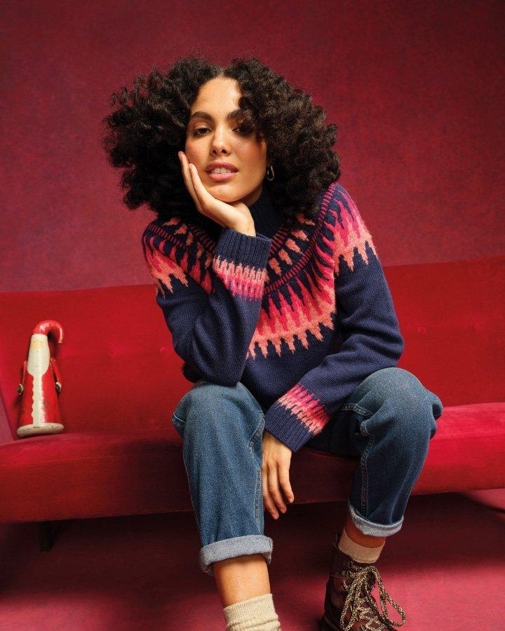 a woman sitting on a red sofa wearing a bright festive knitted jumper with a santa figure next to her