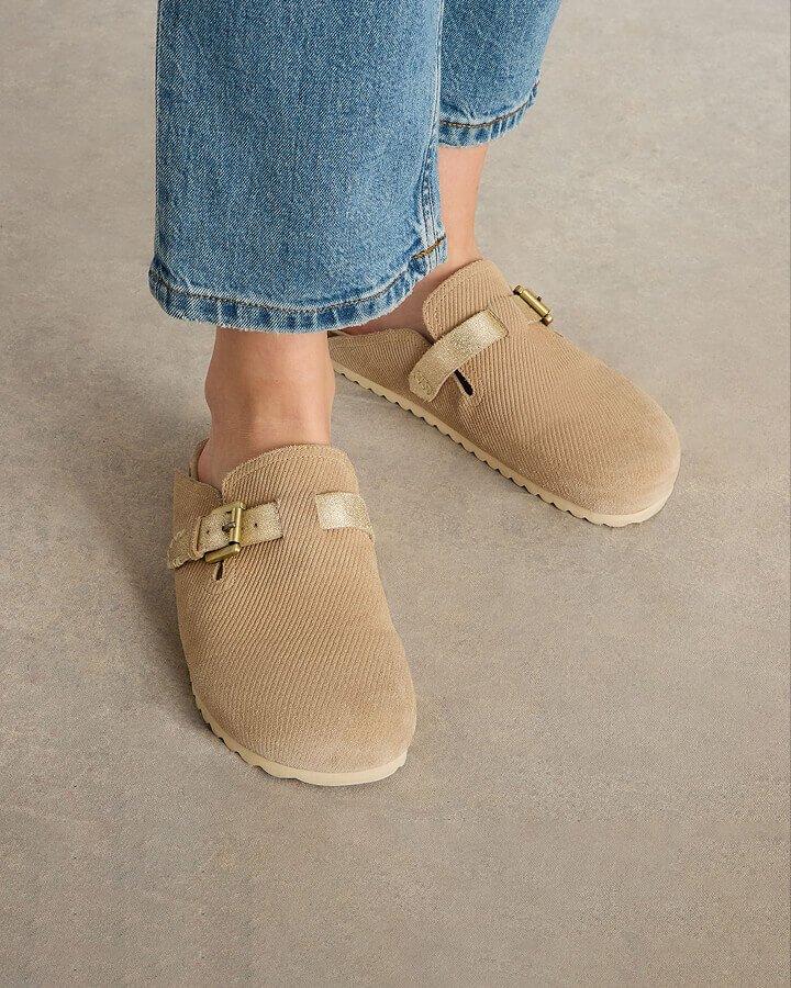 A photo of a woman's feet wearing a pair of beige slip on mules