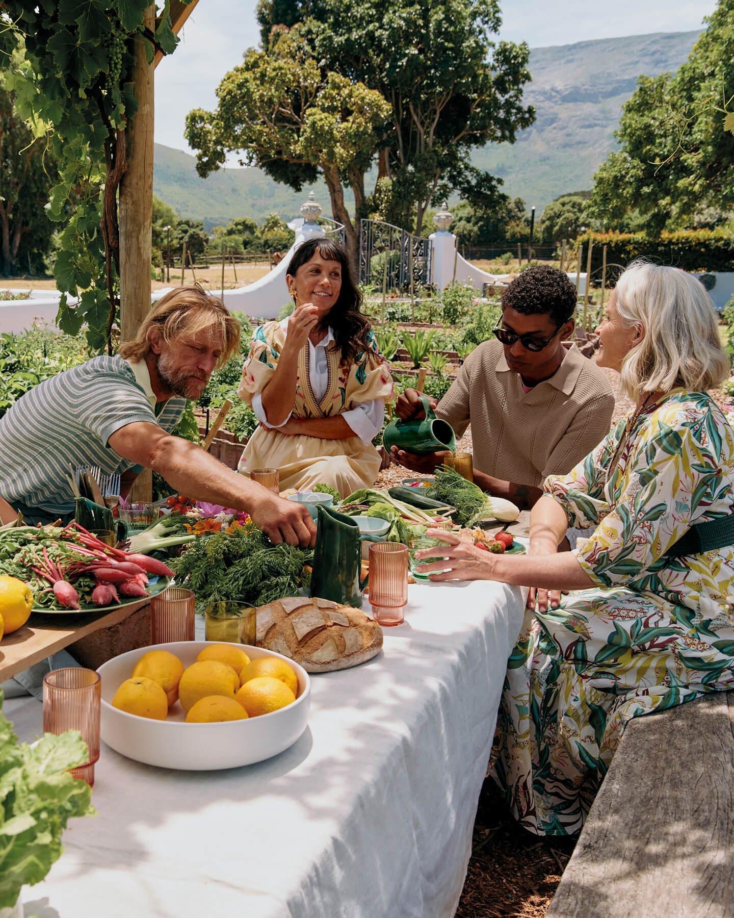 An image of two men and two women sitting around a table in a garden sharing food and drink