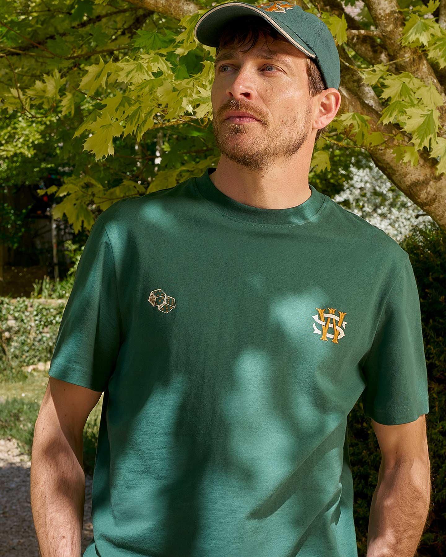 a man in a green shirt and hat standing under a tree
