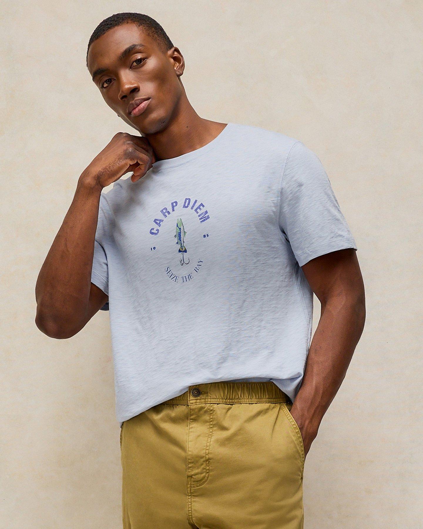 a man in a t-shirt and khaki pants leaning against a wall