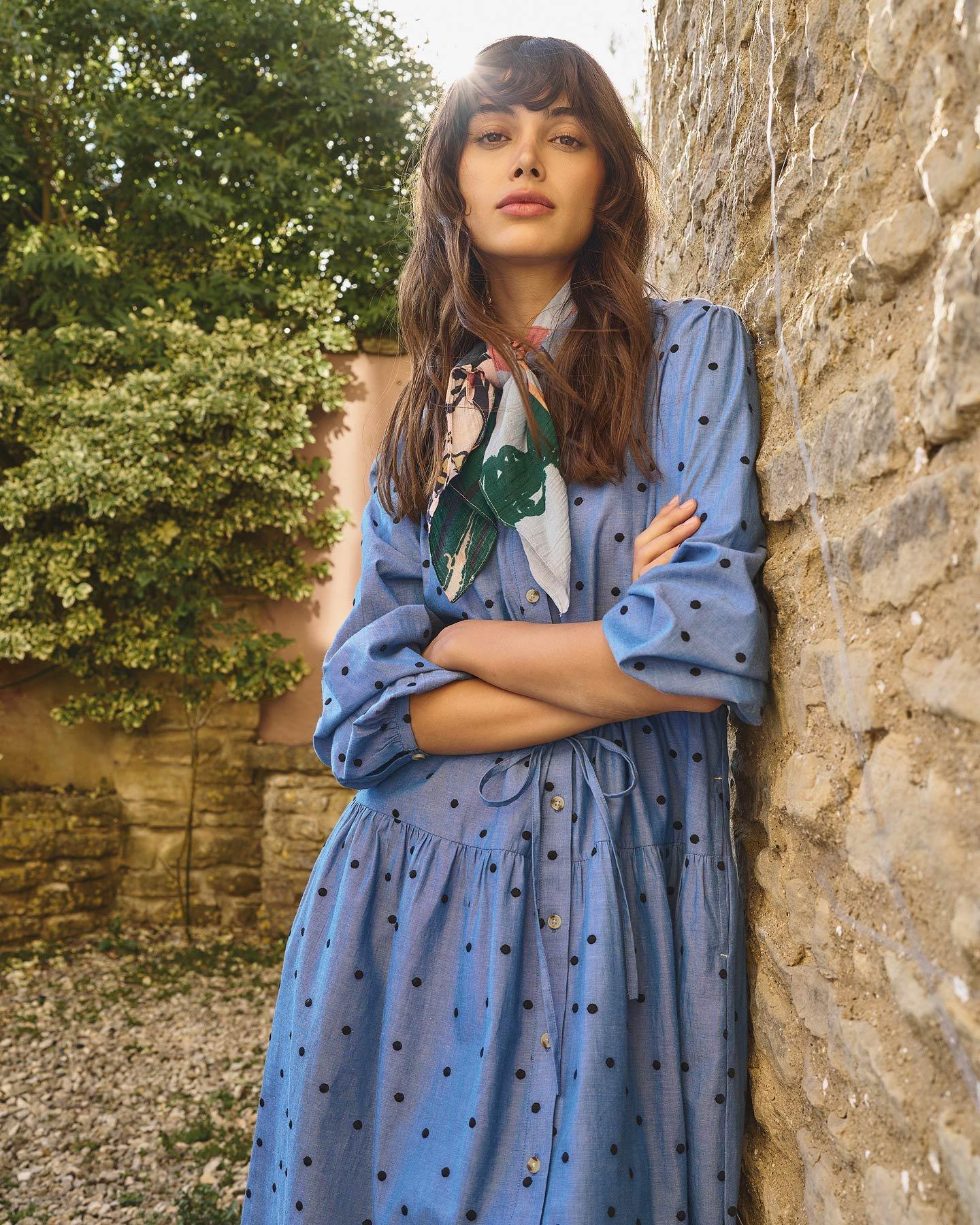 a woman in a blue dress and brown bag standing outside