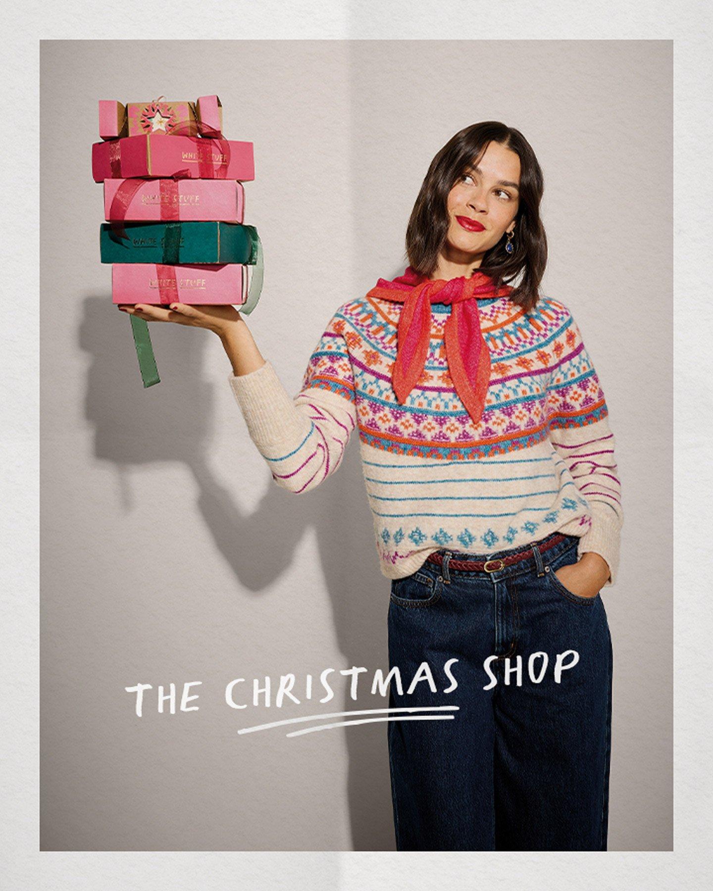a woman holding up a stack of presents with the words the christmas shop