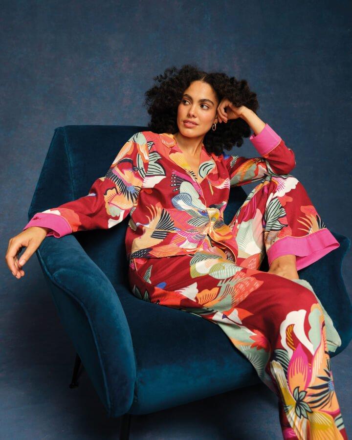 a female model sat on a blue velvet armchair wearing a pink printed pyjama set.