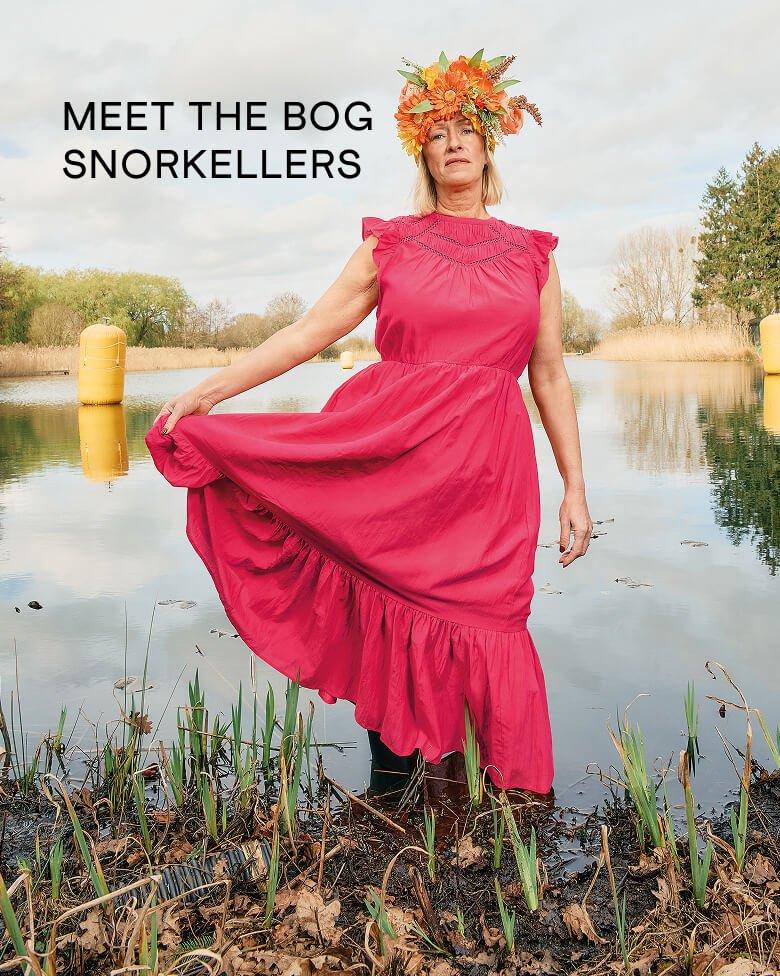 A female model stood in water wearing White Stuff's Paige maxi dress in pink which has been styled with a flower crown atop the models head.