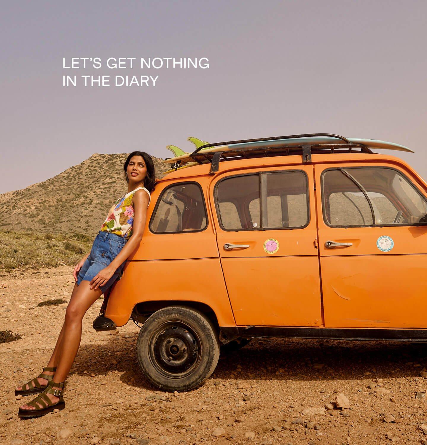 a female model leaning on an orange car wearing White Stuff's combat denim shorts and paradise cotton vest in ivory multi.