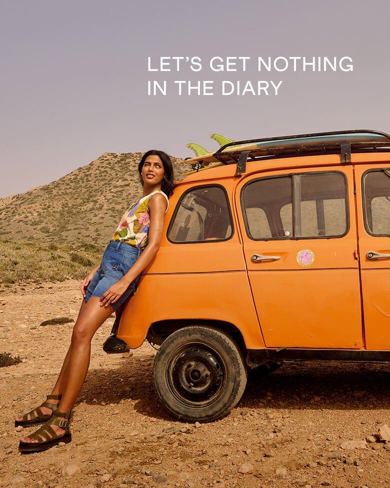 a female model leaning on an orange car wearing White Stuff's combat denim shorts and paradise cotton vest in ivory multi.