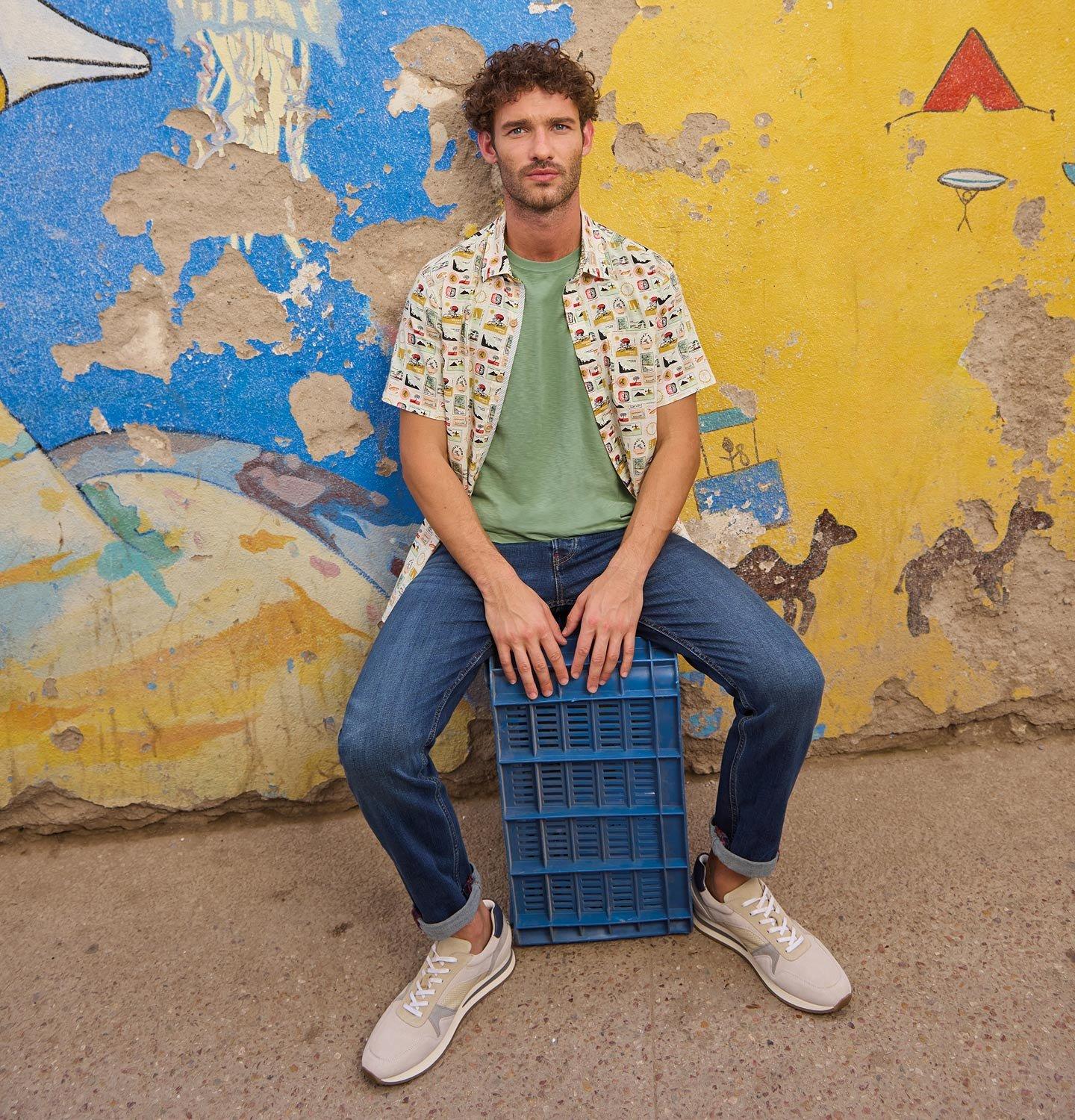 a man sitting on a blue crate in front of a wall wearing the Finsbury printed shirt