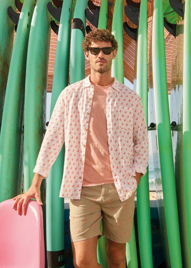 a man standing next to a pink chair in front of a row of surfboards