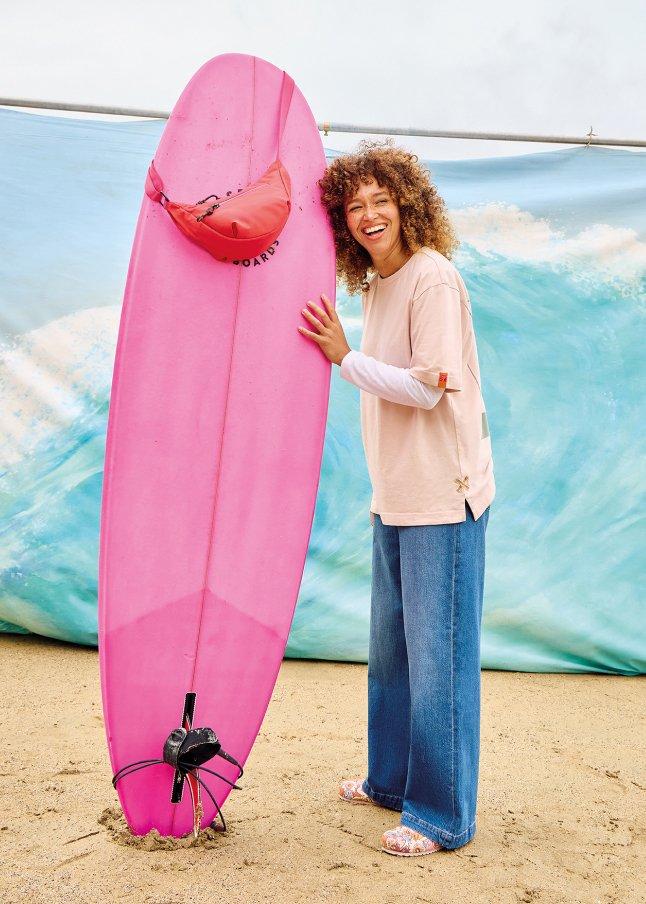 a woman holding a pink surfboard on a beach