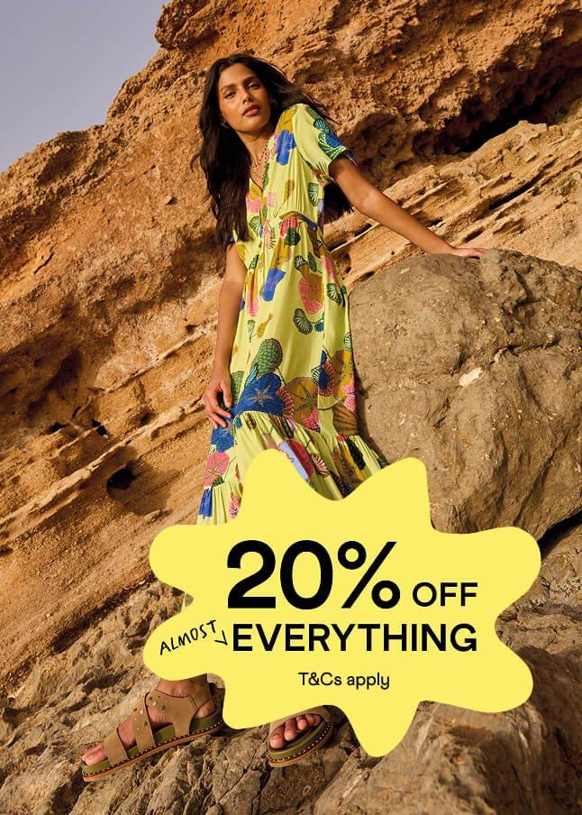 a woman in a yellow dress standing on a rock with a 20 % off everything sign
