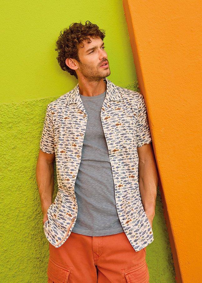 a man leaning against a wall with his hands in his pockets